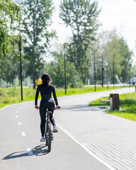 Rear view of Caucasian woman riding bike in park. Vertical photo. 