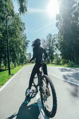 Obraz premium Rear view of Caucasian woman riding bike in park. Vertical photo. 