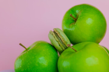 Apple macaroons.Apple sweet pastries and desserts. Macarons with apple aroma and taste.Green macaroons and green apples on a pink background.French pastries.Fruit pastries with apple aroma and cream. 
