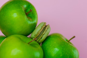 Green macaroons and green apples on a pink background. Apple macaroons.Apple sweet pastries and desserts. Macarons with apple aroma and taste.French pastries.Fruit pastries with apple aroma and cream