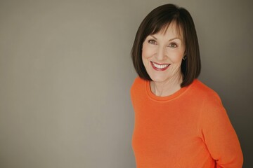 Fototapeta premium Smiling woman in bright orange sweater poses against neutral background in studio setting