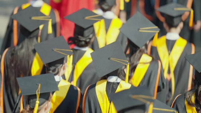 A group of graduates wearing caps and gowns are walking down a street. Scene is celebratory and proud, as the graduates are wearing their graduation attire and walking together