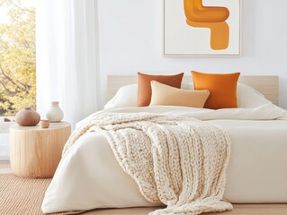 Cozy bedroom with a chunky knit blanket in cream tones, a beige bedspread, terracotta accent pillows, a wooden side table, abstract wall art