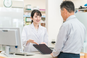 Obraz premium 薬局でタブレットPCを使いながら説明する薬剤師・調剤師（レセコン・レセプトコンピュータ） 