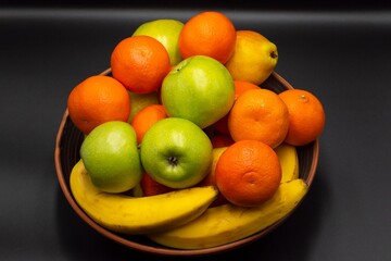 Fresh ripe fruits in a bowl on a gray background. Fruit mix of tangerines, pears, bananas, apples. Healthy eating. Vitamins.