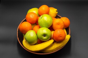 Fresh ripe fruits in a bowl on a gray background. Fruit mix of tangerines, pears, bananas, apples. Healthy eating. Vitamins.