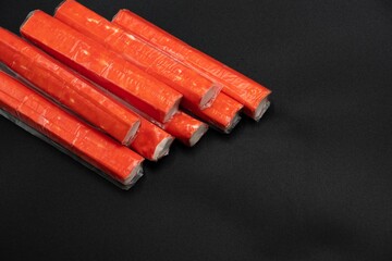 Crab sticks on a black background with space for text laid out in a row © Olha