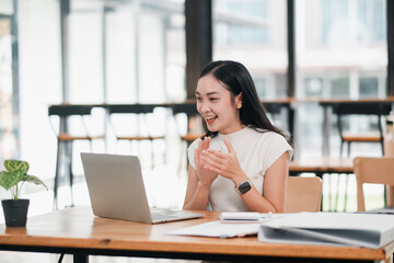 A young woman enthusiastically participates in a video call on her laptop in a bright, modern...