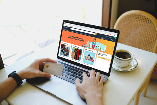 Bangkok, Thailand. January 23, 2025; A person shopping online on Amazon's website via laptop while holding a credit card, with a coffee cup nearby.