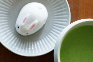 Cup of fresh matcha tea, green tea and Bunny Rabbit shape daifuku Japanese confectionery on wooden table.