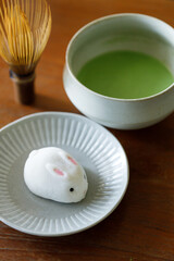 Cup of fresh matcha tea, green tea and Bunny Rabbit shape daifuku Japanese confectionery on wooden table.