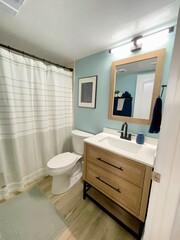 Newly remodeled small bathroom. A modern coastal guest bathroom with white countertop, oak vanity, and beachy wood floors. 