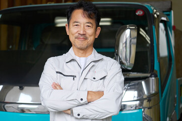 トラックの前に立つ男性作業員のポートレート　カメラ目線
