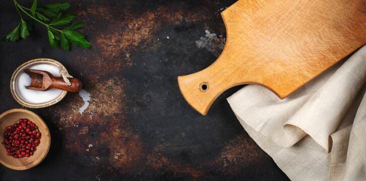 Top view of rustic kitchen background with wooden cutting board, salt, red peppers and parsley.