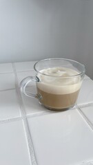 Clear coffee mug with coffee in it on a white tile table with a white background, Copy space