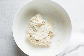 Overhead view of bread dough in a white mixing bowl, dough rising in a ceramic bowl, process of making artisan bread