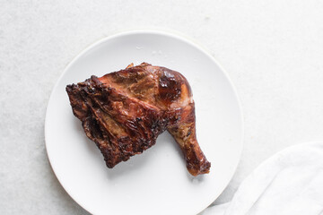 top view of smoked chicken thigh on a white ceramic plate, overhead view of smoked chicken leg