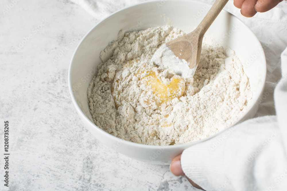 Sticker mixing flour into vanilla cookie dough in a white mixing bowl, plain vanilla cookie dough about to be baked, process of making vanilla cookie dough