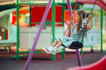 Little Girl Swings Peacefully and Safely Enjoying Playtime. Lonely kid having fun alone at the playground 

