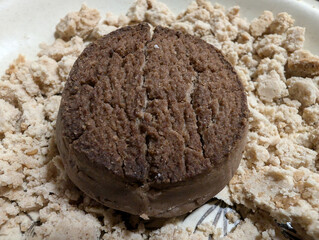 Macro view of traditional Spanish Christmas chocolate polvorón dessert with crumbled and broken almond butter cookie. Detailed texture and scattered crumbly pieces, appetizing classic treat sample. 