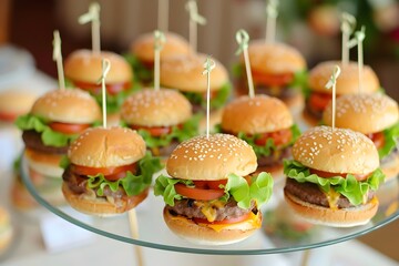 A display of mini burgers on a glass plate, arranged in an elegant and visually appealing way. The burger buns have a golden color from the grill or baking process, each with perfectly cut lettuce lea