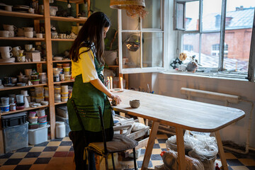 Thoughtful woman potter prepare clay for shaping pottery in workshop. Female artisan focused on craft, set material, tactile process, art creation. Clay preparation, shaping techniques, pottery class