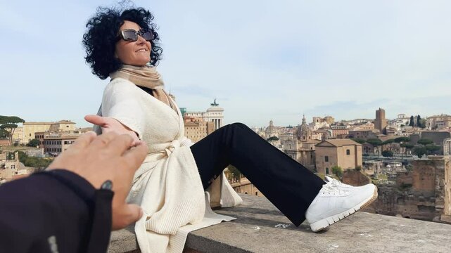 Tourist woman is sitting on a ledge at Belvedere terrace at Palatino hill sightseeing the Roman Forum panoramic view in a city or Rome.. Female is enjoying the view