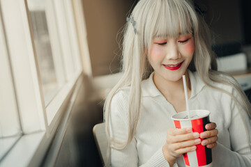 woman with long, light hair enjoys drink while sitting by window