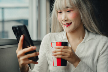 Enjoying drink while using smartphone, woman with long hair smiles