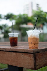 A glass of iced Thai milk tea and black coffee background in the plastic cup after drink finishes on wood table at garden cafe
