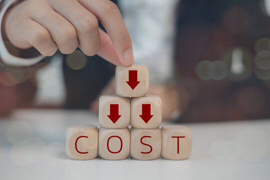 Cost reduction concept. The cost reduction concept affects product cost, profit, inflation, and the economy's recession. Hand puts wooden cube with words cost and red down arrows. business improvement