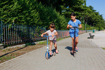 two girls riding push scooters on a sunny day