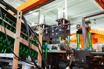 Machine assembling green glass bottles in a factory during daylight hours