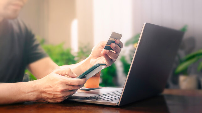Man using laptop and smartphone for online shopping with credit card to pay online on virtual screen application. Smart e-commerce, Internet payment, Financial technology concept.