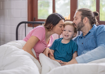 Fototapeta premium Family enjoying a cozy morning together in bed with warm blankets and natural light