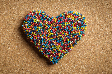 Fototapeta premium A heart crafted from colorful push pins on a corkboard, postcard design. Valentine concept