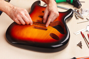 Guitar technician measures size of holes for tremolo in body of guitar with ruler.