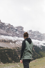 Fototapeta premium Hiker, with his back to the camera, admires the snow-capped mountains of the Aragonese Pyrenees on the famous Cola de caballo route.