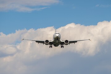 Airplane approaches landing at a busy airport under a blue sky with fluffy white clouds in the background