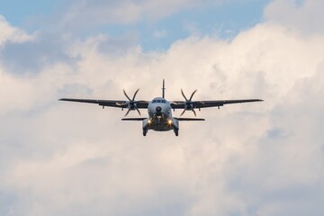 Military aircraft approaches for landing under a cloudy sky during daylight hours in a serene environment