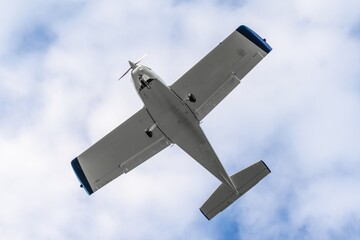 Small aircraft flies overhead against a backdrop of soft clouds in a clear blue sky on a sunny day