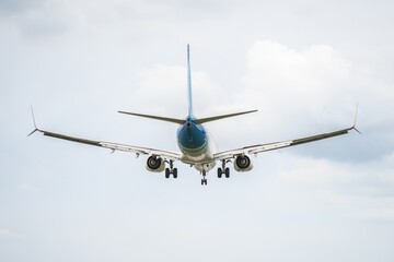 Jet aircraft approaches landing at an airport under a cloudy sky with visible landing gear