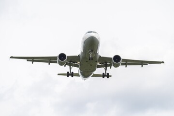 Airplane approaches landing at an airport against a cloudy sky in an urban environment. 