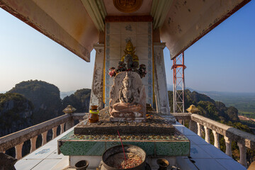 Fototapeta premium Small Buddha statue on the altar and the surrounding mountainous area behind it on top of the mountain at the Tiger Cave Temple (Wat Tham Suea (Sua)) in Krabi, Thailand, on a sunny day.