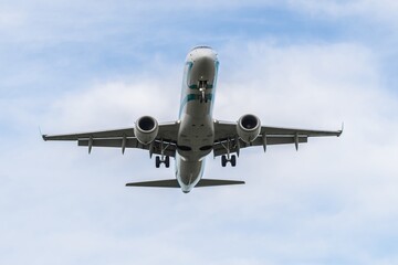Airplane flying overhead on a clear day with a backdrop of blue skies and scattered clouds