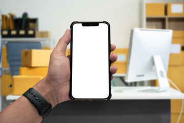 Hand holding white mobile phone with blank white screen in office.