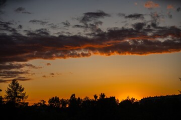Vibrant sunset casting warm hues over trees and landscape in a tranquil evening sky