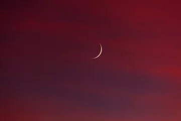 A crescent moon is shining brightly in the sky above a red background