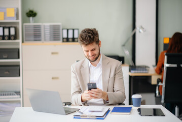 Obraz premium Confident businessman working on finance analysis with a tablet and laptop at office desk.
