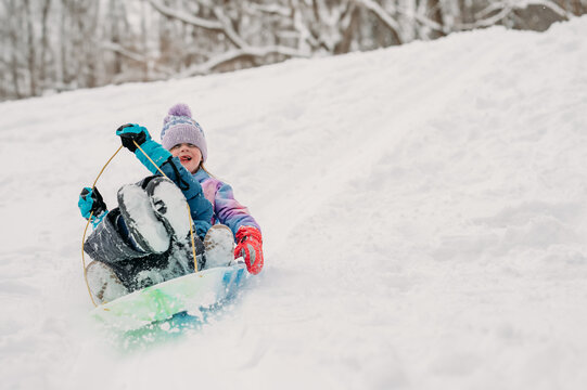 Child in winter gear sledding down a snowy hill with excitement.